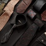 Flat lay of a black dress shirt, colorful ties, and accessories for men's formal wear.