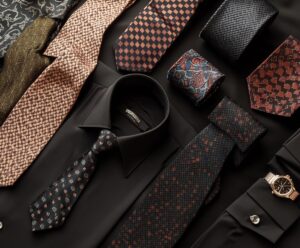 Flat lay of a black dress shirt, colorful ties, and accessories for men's formal wear.